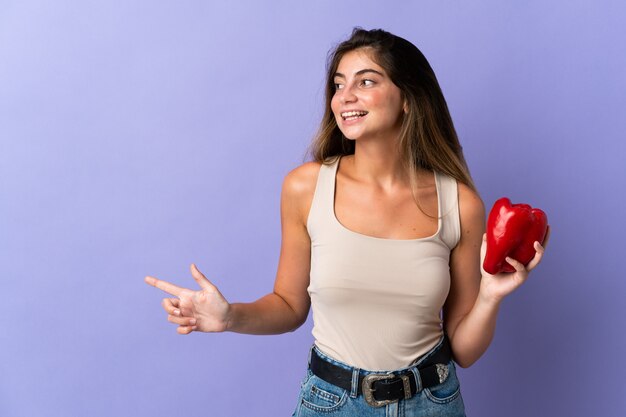 Jonge vrouw die een peper houdt die op purper wordt geïsoleerd richtend aan de kant om een product voor te stellen