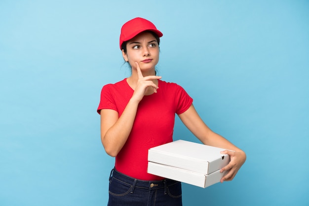 Jonge vrouw die een pizza over geïsoleerde roze muur houdt die een idee denkt