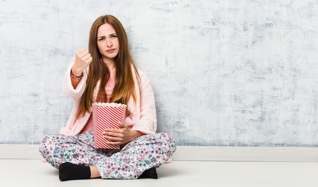 Jonge vrouw die een popcornemmer houdt die vuist toont