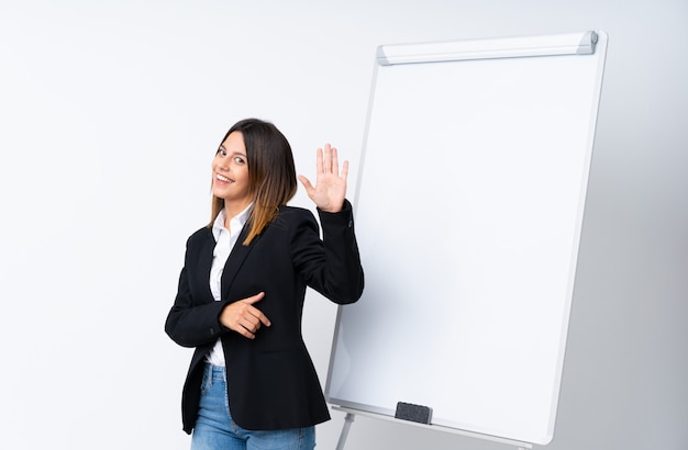 Jonge vrouw die een presentatie op wit bord geven die met hand met gelukkige uitdrukking groeten