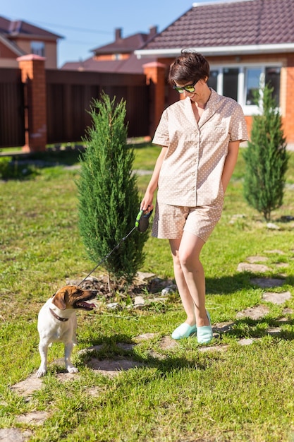 Jonge vrouw die een pyjama draagt met haar hond op de achtertuin, het concept van dieren en vriendschap of huisdier bezit