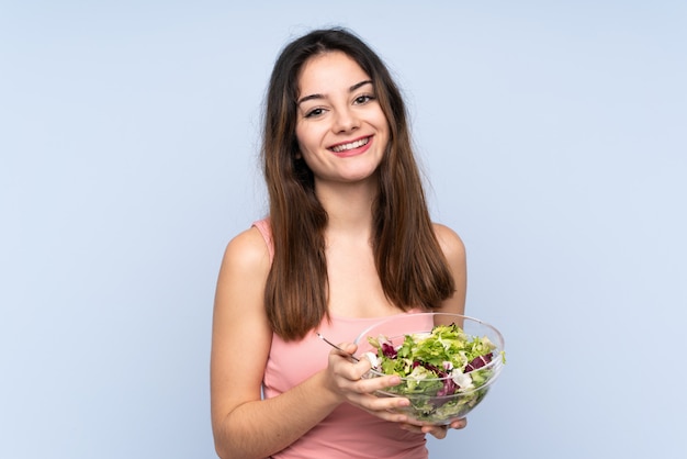 Jonge vrouw die een salade op blauw houdt