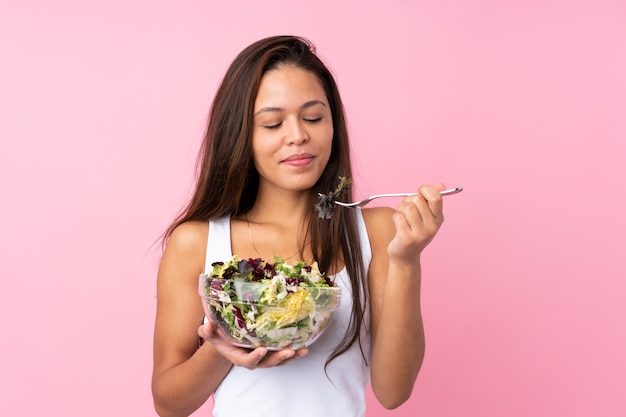 Jonge vrouw die een salade over geïsoleerde muur houdt