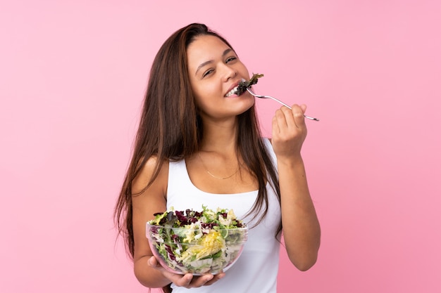 Jonge vrouw die een salade over geïsoleerde muur houdt