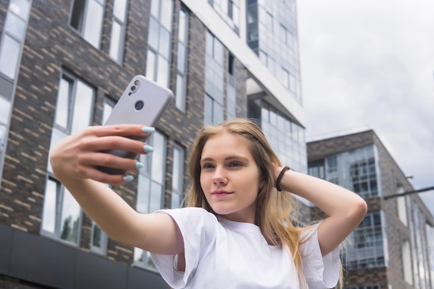 Jonge vrouw die een selfie maakt of een spiegel-app gebruikt op straat tegen de achtergrond van moderne gebouwen