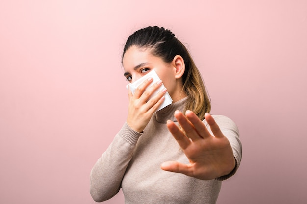 Jonge vrouw die een servet houdt als virus beschermend masker en opgeheven hand die vraagt om afstand te houden