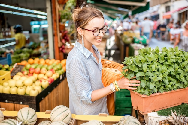 Jonge vrouw die een verse munt kiest die zich met mand bevindt bij de voedselmarkt in Frankrijk