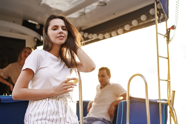 Jonge vrouw die een wijnglas vasthoudt en op het dek van een zeiljacht zit