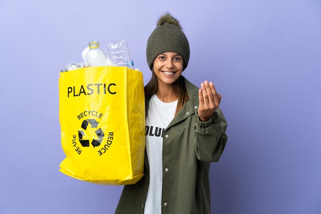 Jonge vrouw die een zak vol plastic houdt die uitnodigt om met de hand te komen. Blij dat je gekomen bent