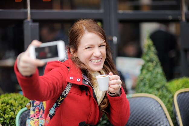 Jonge vrouw die een zelfportret (selfie) met slimme telefoon in een Parijse straatkoffie neemt