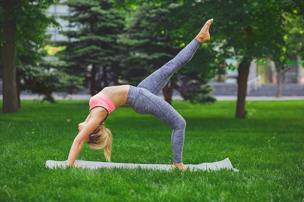 Jonge vrouw die eenbenig wiel maakt Pose buitenshuis in het park, kopieer ruimte. Jong slank meisje maakt oefening. Stretching, wellness, kalmte, ontspannen, gezond, actief levensstijlconcept