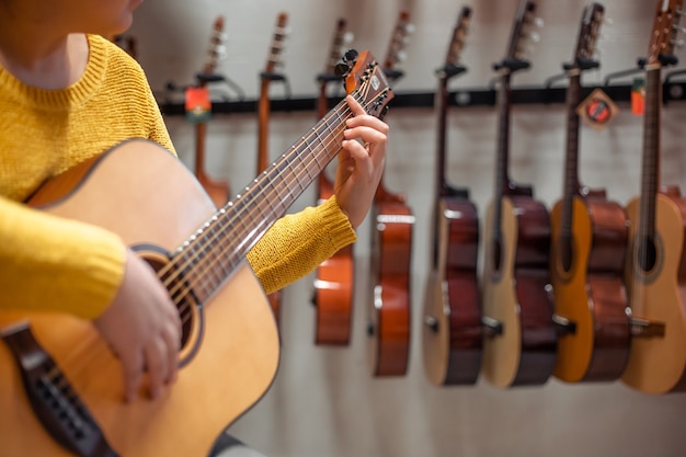 Jonge vrouw die en een nieuwe houten gitaar in instrumentale of muzikale winkel, instrumentconcept probeert te kopen