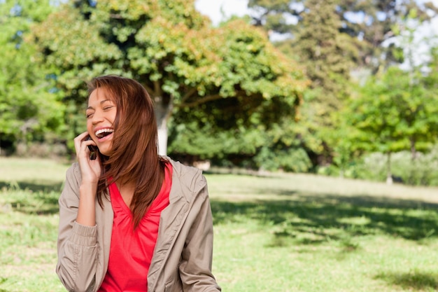 Foto jonge vrouw die enthousiast terwijl op de telefoon op een open weidegebied lacht