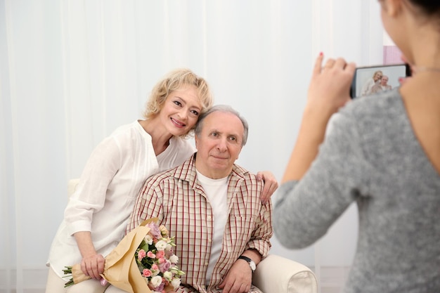 Jonge vrouw die foto's maakt van een gelukkig senior paar thuis