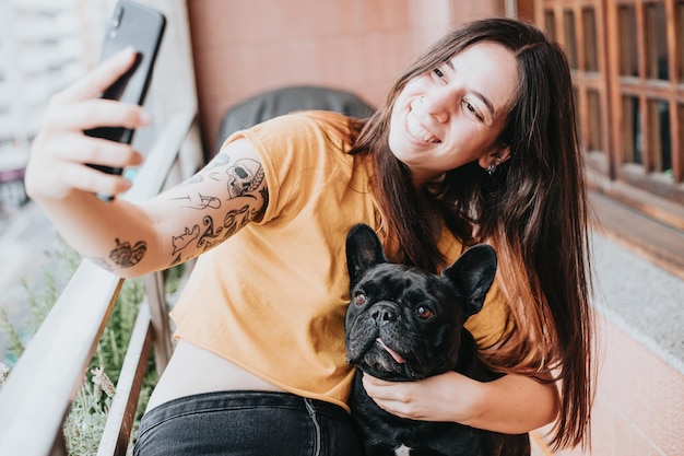 Jonge vrouw die foto selfie knuffelt en voor haar franse bulldog zorgt met tong uit op huisPuppy observeert geconcentreerd kijkend naar de stad Speelshumoristische en vrolijke vriendschapspartner