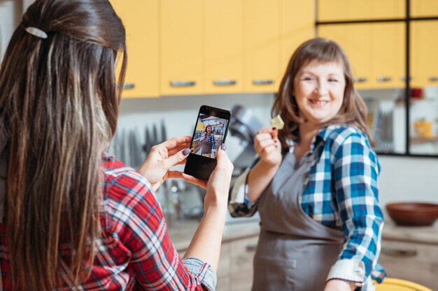 Jonge vrouw die foto van een andere dame in keuken neemt tijdens het koken