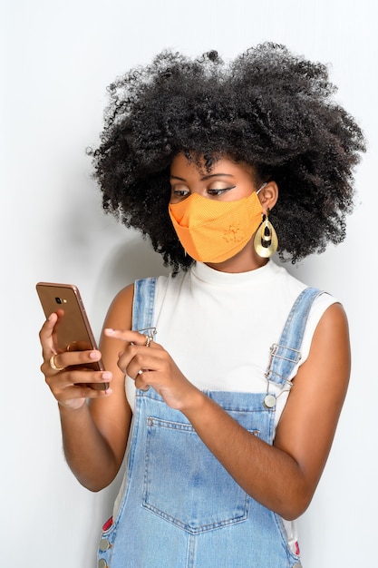 Jonge vrouw die gezichtsbeschermingsmasker gebruikt en een bericht versturen met mobiel
