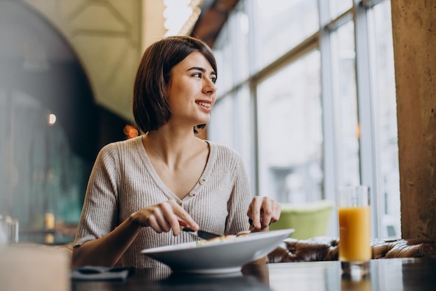 Jonge vrouw die gezond ontbijt met sap eet in een café