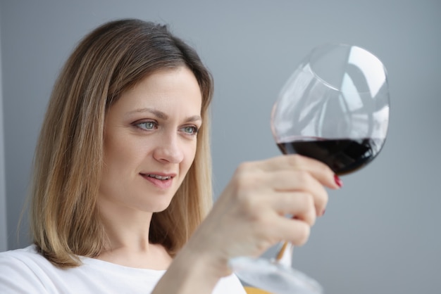 Jonge vrouw die glas met rode wijn onderzoekt