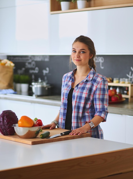 Jonge vrouw die groenten snijdt in de keuken bij het bureau