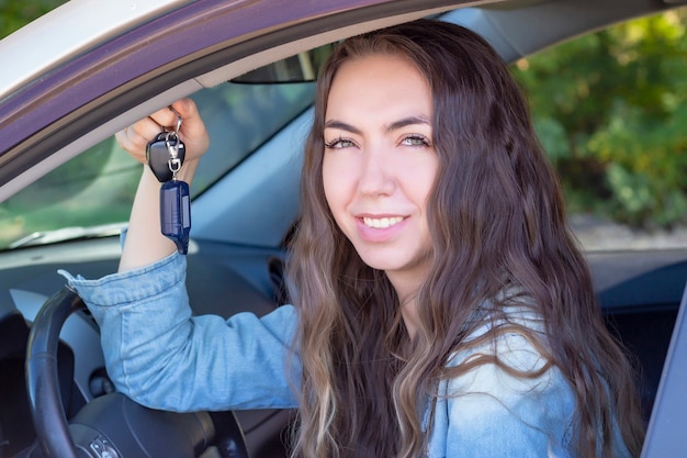 Jonge vrouw die haar auto drijft. aantrekkelijke jonge meisjesbestuurder in nieuwe auto. meisje kocht een auto. toont de sleutels van een nieuwe auto