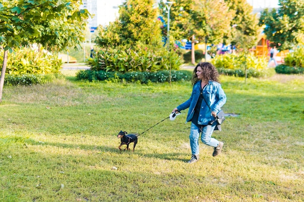 Jonge vrouw die haar hondje buiten speelt en traint. Black and Tan dwergpinscher vrouwelijke hond met eigenaar in een park