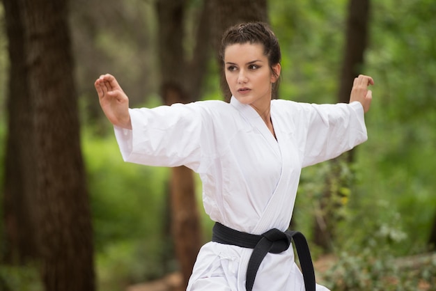 Jonge vrouw die haar karatebewegingen beoefent in bebost bosgebied Witte kimono zwarte band