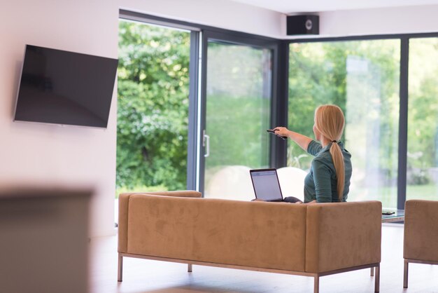 Jonge vrouw die haar laptopcomputer gebruikt in haar luxe moderne huis, glimlachend