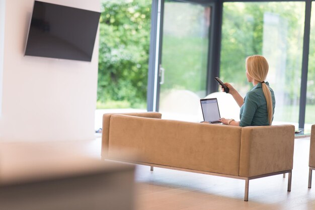 Jonge vrouw die haar laptopcomputer gebruikt in haar luxe moderne huis, glimlachend