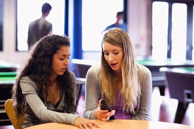 Jonge vrouw die haar mobiele telefoon toont aan een vriend