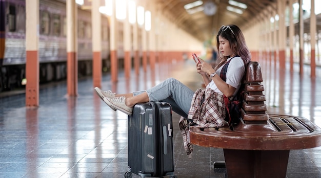 Jonge vrouw die haar smartphone gebruikt terwijl ze op de trein wacht op een treinstation.