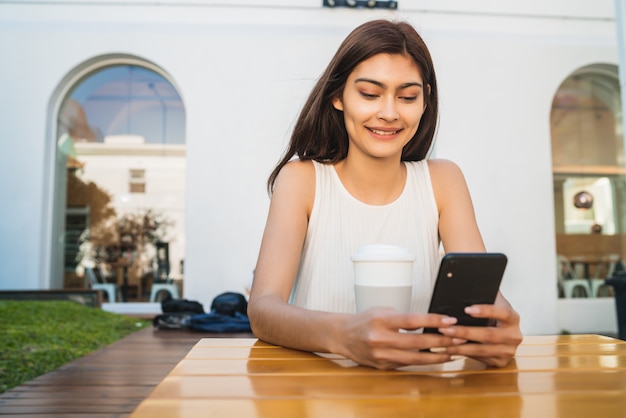 Jonge vrouw die haar telefoon met behulp van bij koffiewinkel.