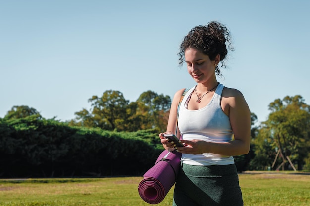 jonge vrouw die haar telefoon sms't en met een roze yogamat