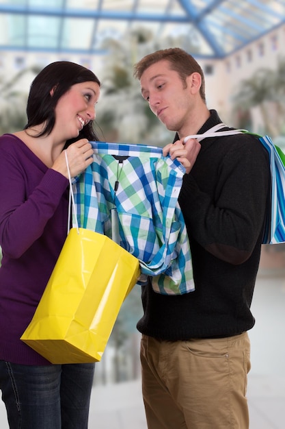 Foto jonge vrouw die haar vriend een shirt laat zien tijdens het winkelen in een winkelcentrum