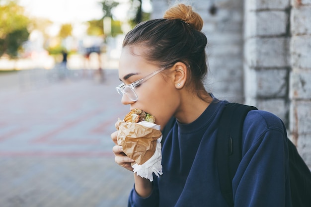 Jonge vrouw die hamburger eet op straat.