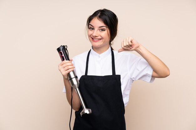 Jonge vrouw die handmixer over trots en zelfverzekerde muur gebruiken