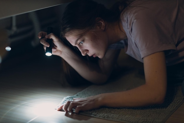 Jonge vrouw die handzaklamp in duisternis houdt en vuil op tapijt zoekt