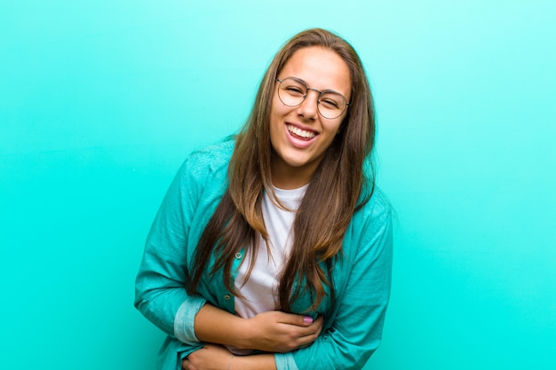 Foto jonge vrouw die hardop bij sommige hilarische grap lacht, zich gelukkig en vrolijk voelt, hebbend pret tegen blauwe achtergrond