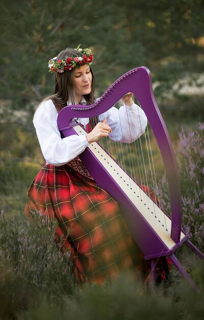 Foto jonge vrouw die harp speelt in het bos.