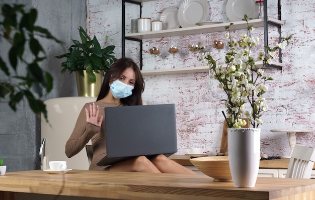 Foto jonge vrouw die het masker van het beschermingsgezicht draagt die laptop voor videogesprek thuis met behulp van