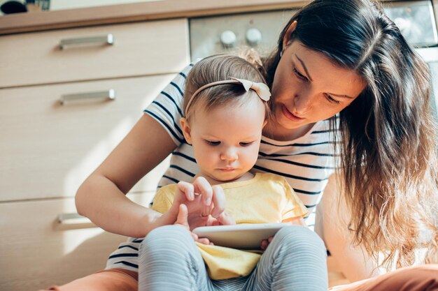 Jonge vrouw die het scherm van een smartphone aanraakt terwijl haar peuterdochter het vasthoudt