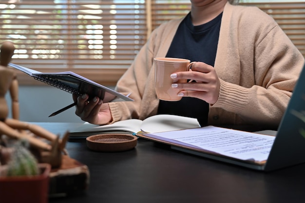 Jonge vrouw die hete koffie drinkt en 's ochtends thuis een boek leest.