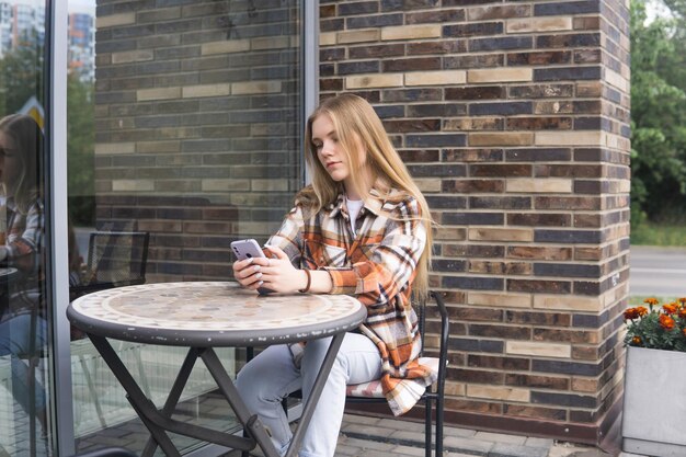 Jonge vrouw die iets aan de telefoon typt terwijl ze aan een cafetariatafel zit