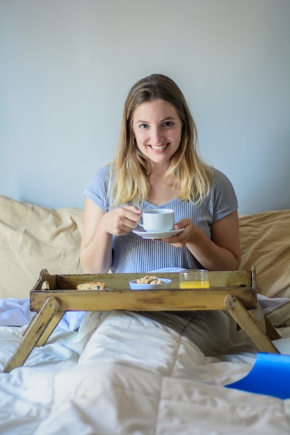 Jonge vrouw die in bed ontbijt eet