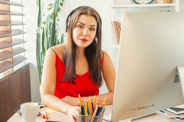 Jonge vrouw die in bureau werkt dat computer met behulp van, die bij bureau zit