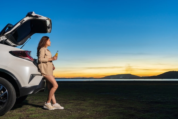 Jonge vrouw die in de buurt van een auto staat en geniet in het veld bij zonsondergang