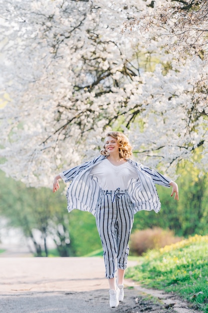 Foto jonge vrouw die in de gebloeide tuin in de lente springt. meisje onder sakura-bloesemboom.