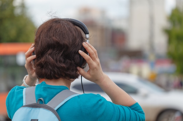 Jonge vrouw die in de stad achterlicht het luisteren muziekhoofdtelefoons loopt