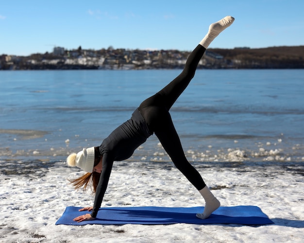 Jonge vrouw die in de winter op het strand buiten yoga beoefent