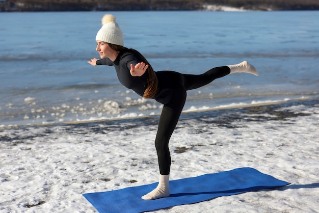 Jonge vrouw die in de winter op het strand buiten yoga beoefent